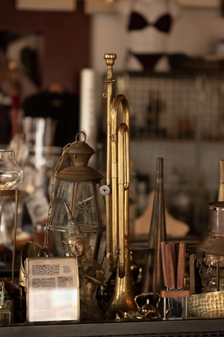A collection of vintage items and antiques displayed, including a brass instrument resembling a trombone, a decorative lantern, a small statue of a deity, and various other brass objects.