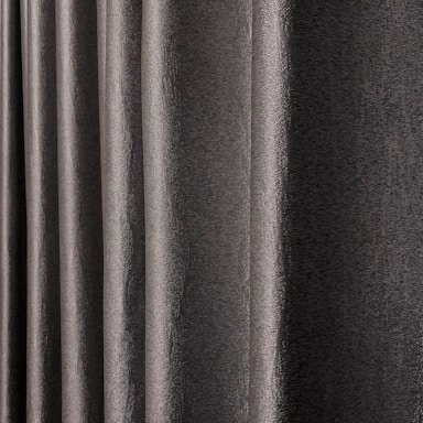 A close-up view of dark, textured drapery fabric with waves and folds creating a sense of movement. The material appears slightly shiny, indicating a smooth finish.