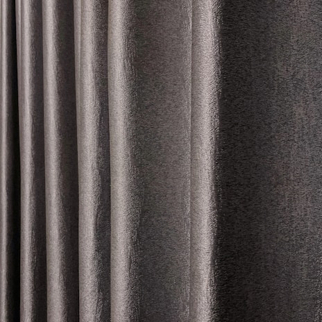 Vertical folds of a dark gray, textured fabric, resembling curtain pleats, evenly spaced.
