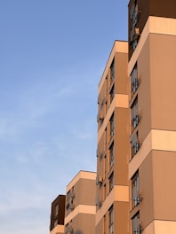 Several modern residential buildings with multiple floors and large windows are positioned under a clear blue sky. The sunlight casts warm tones on the facades, creating an interplay of light and shadows.