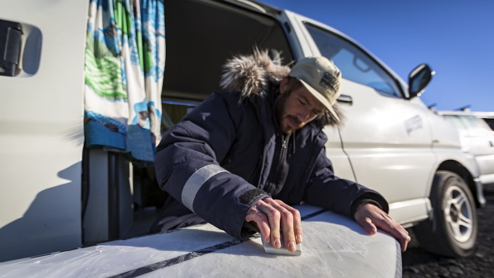 a man with a hat and a jacket on putting a surfboard into a van