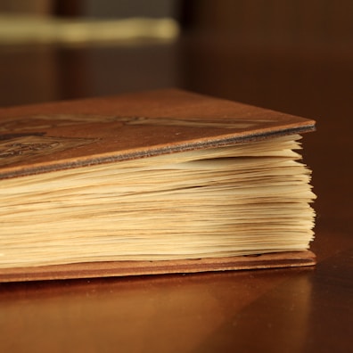 Close-up of a vintage book with a worn leather cover resting on a rustic table.
