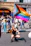 A joyful person holding a rainbow flag in a lively urban neighborhood.
