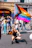A joyful person holding a rainbow flag in a lively urban neighborhood.