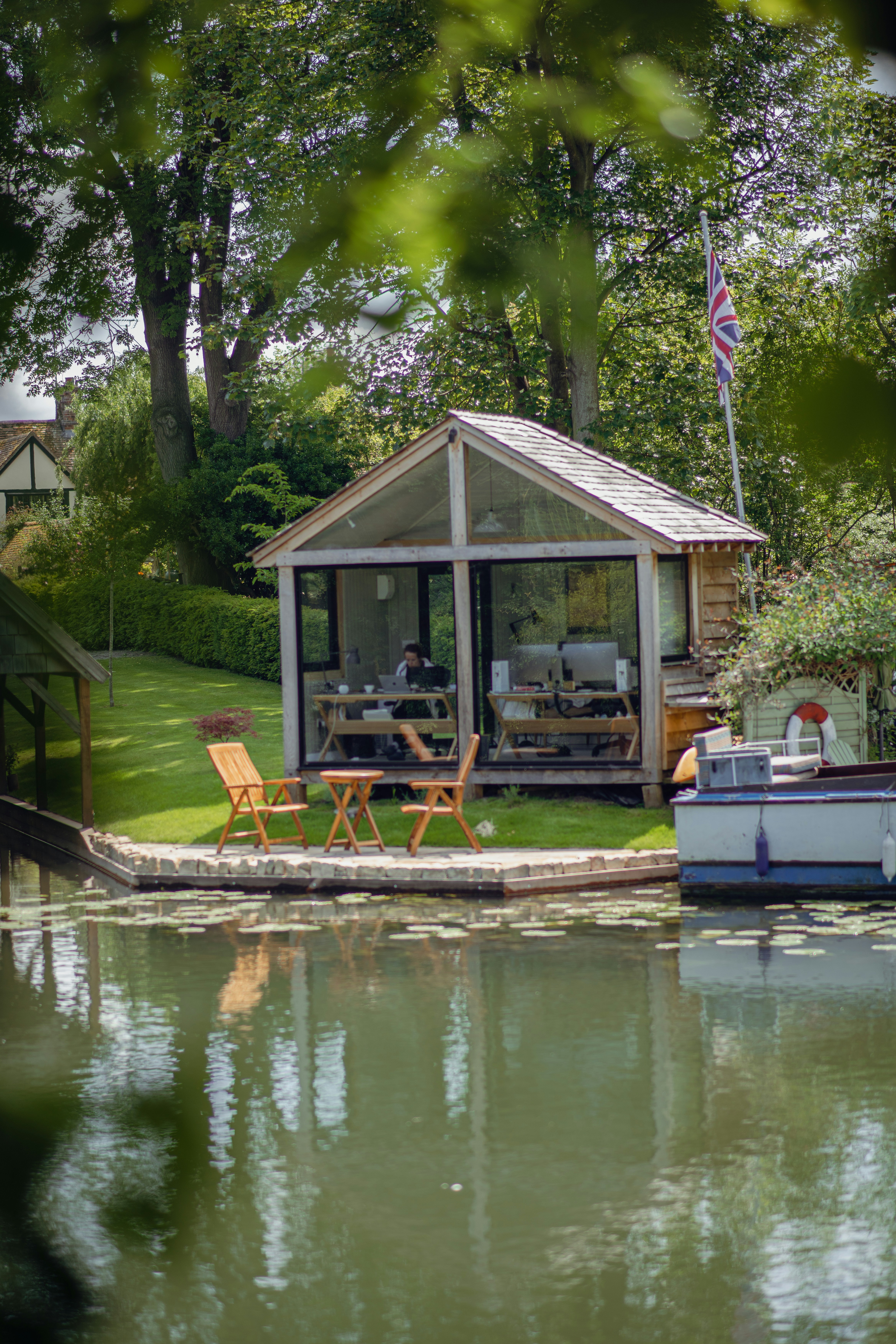 Person working on a laptop inside a garden office by the water.
