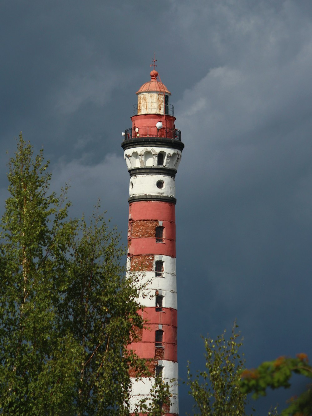 a red and white lighthouse with trees in the foreground
