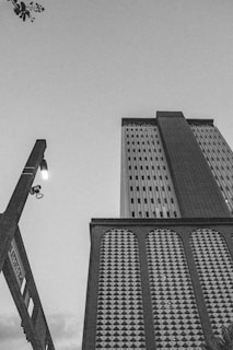 A black and white photograph featuring a tall building with a textured facade and a visible corner. A street sign reads 'Florida,' and a street lamp is illuminated. The sky is clear with a few visible clouds.