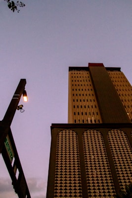 A tall building with a patterned facade is seen from a low angle against a dimly lit sky, creating a dramatic perspective. A streetlight and a street sign indicating 'Florida' are visible to the left. The building's design includes geometric motifs and vertical lines.