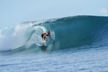 A surfer skillfully rides inside a large, powerful ocean wave. The wave curls above the surfer, creating a natural tunnel. The water is clear and blue, evoking a sense of dynamic motion and energy.