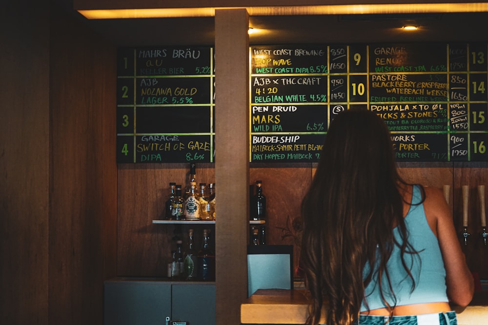 a woman standing in front of a menu behind a bar