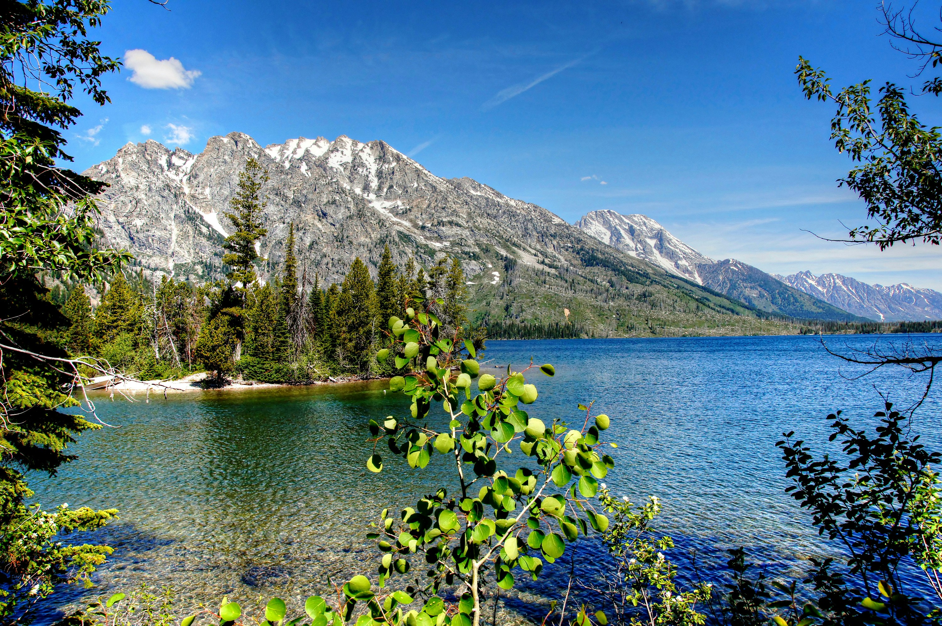 a lake surrounded by trees and mountains under a blue sky, Jenny Lake at Grand Teton National Park - 1589 Grand Teton National Park lies in Northwestern Wyoming about ten miles south of Yellowstone National Park.