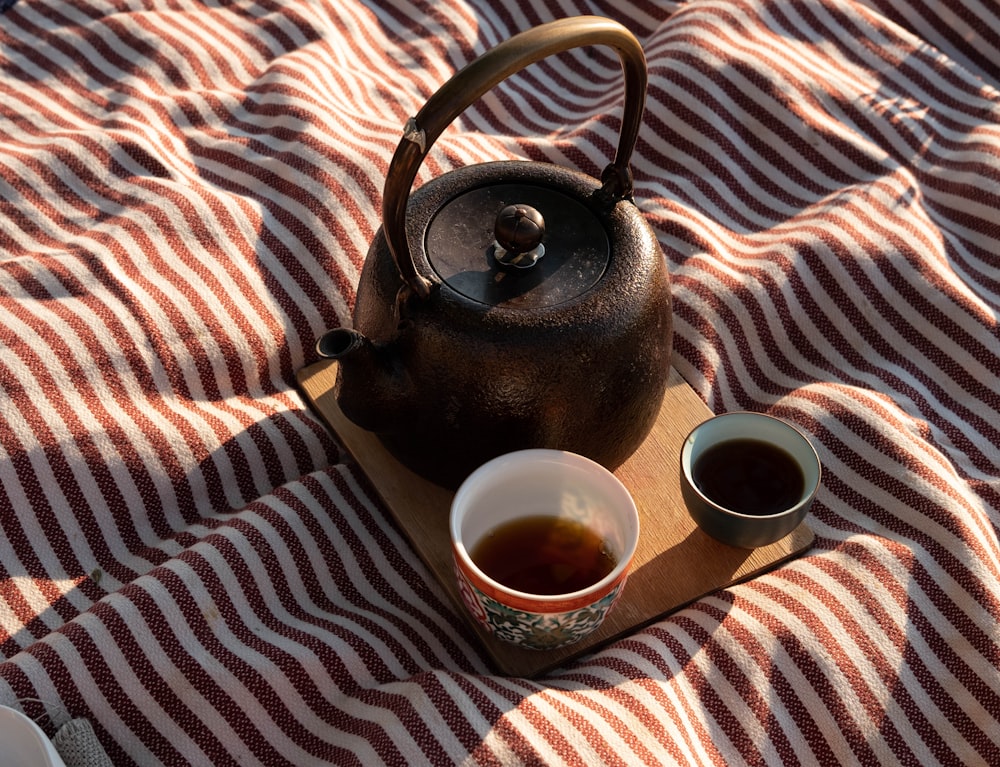 a tea pot and two cups of tea on a blanket