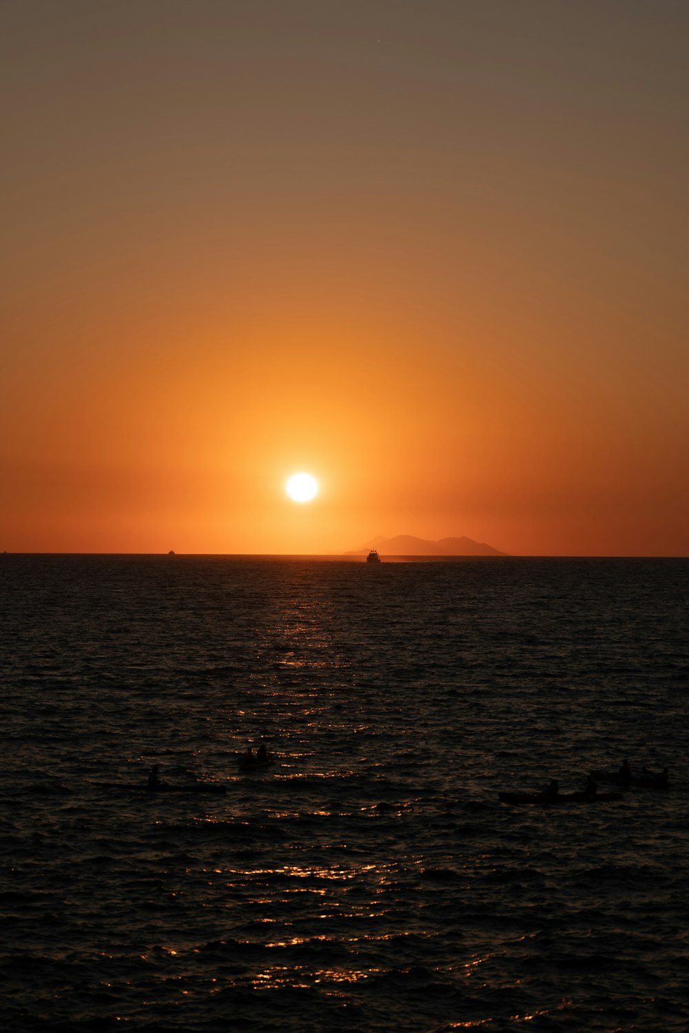 the sun is setting over the ocean with a boat in the distance