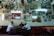 A group of three men sit at a table in a room filled with framed pictures and clocks on the walls. The Turkish flag is prominently displayed. The ceiling is adorned with various lighting fixtures, and the atmosphere is reminiscent of a traditional cafe or gathering space.