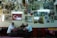 A group of three men sit at a table in a room filled with framed pictures and clocks on the walls. The Turkish flag is prominently displayed. The ceiling is adorned with various lighting fixtures, and the atmosphere is reminiscent of a traditional cafe or gathering space.