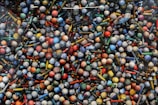 A collection of vibrantly colored balls and variously shaped pin-like objects arranged closely together, creating a visually stimulating pattern. The items display a range of colors including red, blue, yellow, green, and orange.
