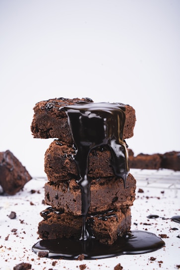 A close-up of a decadent brownie topped with chocolate drizzle and sprinkles on a rustic wooden table.