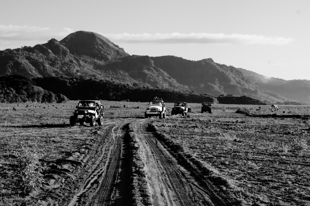a black and white photo of four jeeps on a dirt road