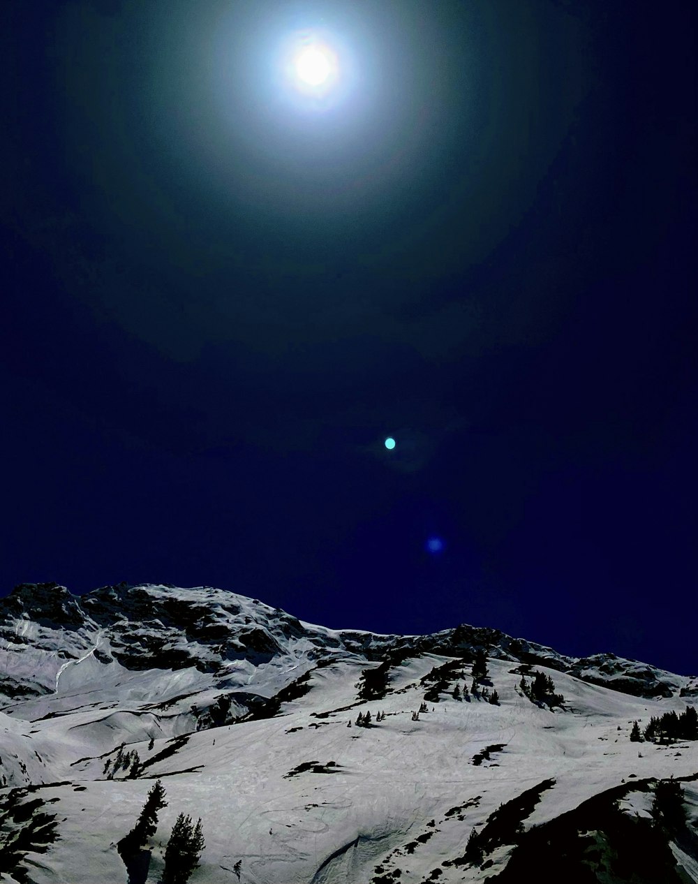 a full moon is seen above a snowy mountain