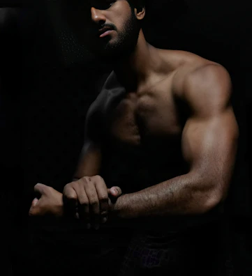 Side profile of a man wearing baggy pump covers, muscles tensed under low light.