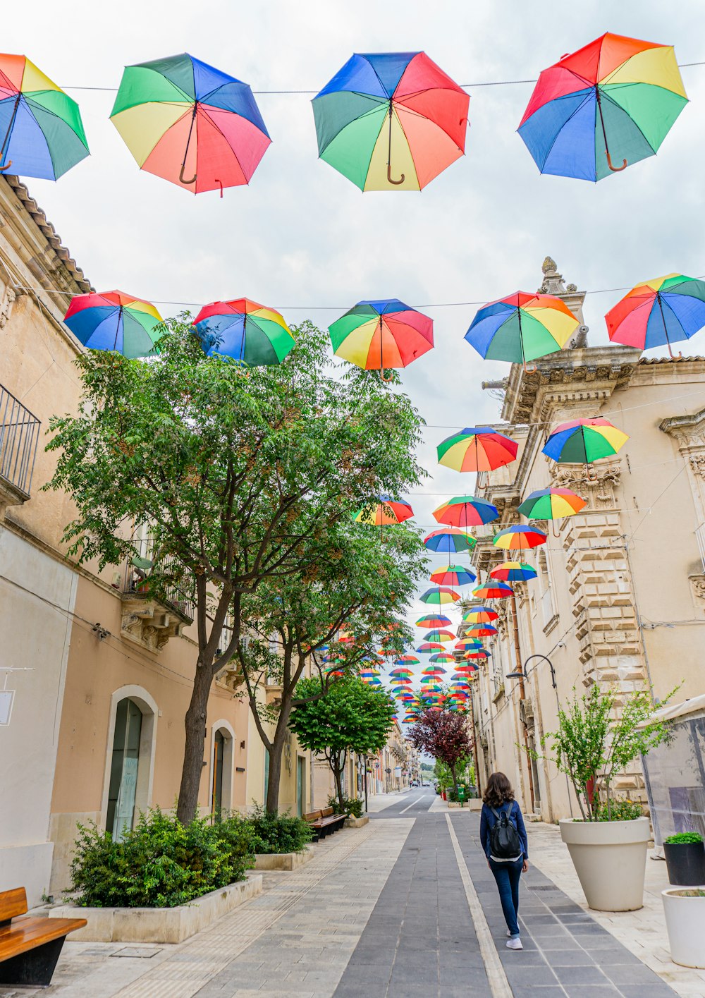 a woman walking down a street under colorful umbrellas