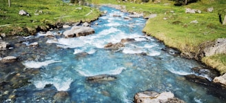 A clear mountain stream winding through natural landscape with charcoal rocks.