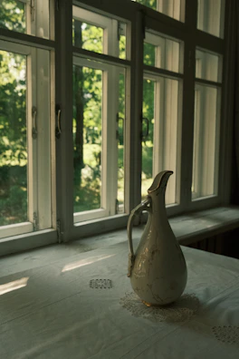 A serene outdoor shot of a stoneware pitcher beside a window, sunlight highlighting its handcrafted details.