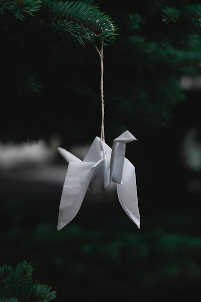 a white origami bird hanging from a pine tree
