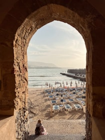 a person sitting on a beach under an archway