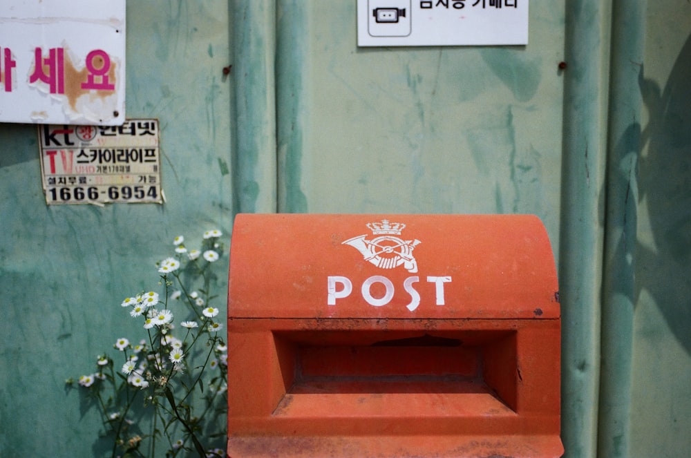 a red post box sitting in front of a green wall