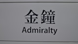 A sign featuring the word 'Admiralty' in English and corresponding Chinese characters on a light gray background.