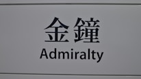 A sign featuring the word 'Admiralty' in English and corresponding Chinese characters on a light gray background.