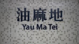 Dark blue Chinese characters and the words 'Yau Ma Tei' in English are prominently displayed on a background of small, square grayish tiles.
