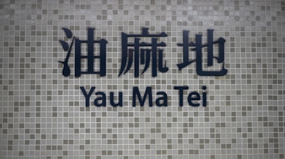 Dark blue Chinese characters and the words 'Yau Ma Tei' in English are prominently displayed on a background of small, square grayish tiles.