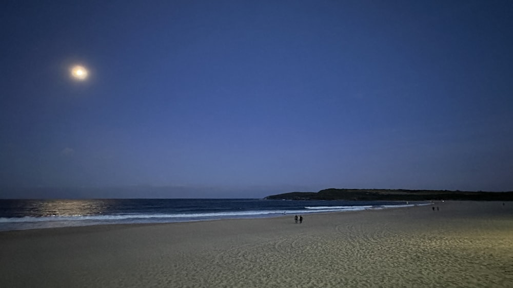 a full moon over a beach with people walking on it