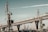A large industrial area featuring several cranes near a port. A modern bridge with a complex steel structure stretches across the scene in the background. The sky has a muted tone, adding to the industrial aesthetic.