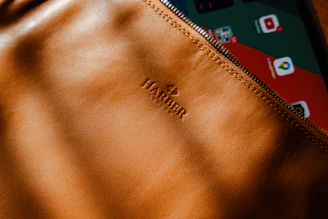 A compact leather mobile pouch with a zipper, placed beside a smartphone on a dark fabric.