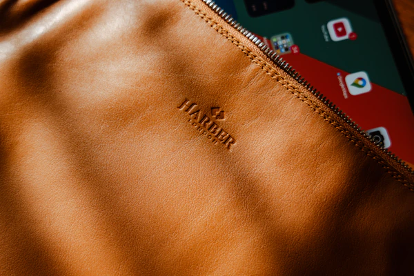 A compact leather mobile pouch with a zipper, placed beside a smartphone on a dark fabric.