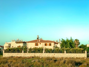 Stone villa exterior surrounded by lush greenery and a clear blue sky.