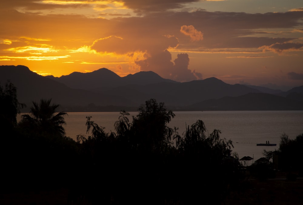 the sun is setting over a lake with mountains in the background