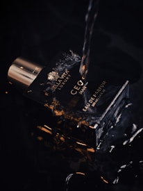 A dark-themed image featuring a bottle of perfume. The bottle has a luxurious design with the text 'CEO MAN' and 'EAU DE PARFUM'. Water droplets and splashes suggest a sense of freshness and vitality. The lighting highlights the sleek, reflective surface of the bottle, creating an elegant and sophisticated aesthetic.