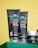 Close-up of three skincare products from the brand mCaffeine placed on a green surface against a yellow background. Two black tubes labeled 'naked & raw coffee face wash' and 'coffee face scrub' are prominently displayed along with a round container, also branded.