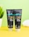 Two black tubes of skincare products are placed on a bright yellow surface against a pale green background. The products are labeled as coffee face wash and coffee face scrub by mCaffeine. A potted plant and a white towel are slightly visible in the background, adding an element of freshness.