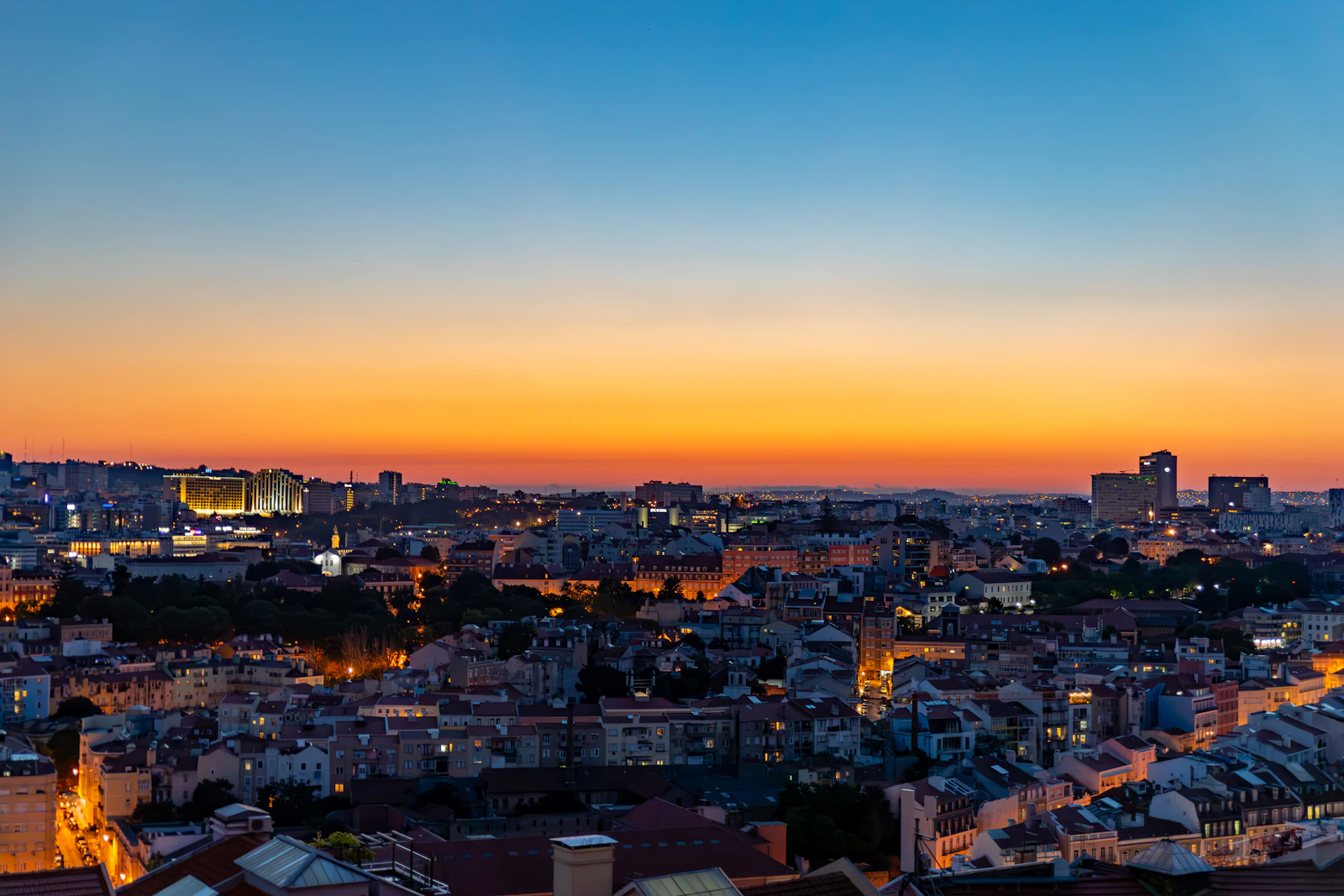 Lisbon city lights at dusk under an orange sky, seen from a hilltop viewpoint, where a Lisbon eSIM keeps maps working
