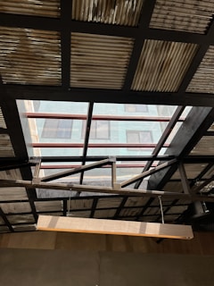 A ceiling with a partially transparent section featuring metal beams and corrugated metal sheets. Sunlight streams through the transparent panels providing a contrast between light and shadow. A wooden beam or light fixture hangs diagonally across the foreground.