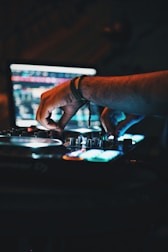Hands mixing beats on a DJ controller in a dimly lit studio.
