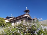 The church exterior framed by blooming spring flowers under a clear blue sky.