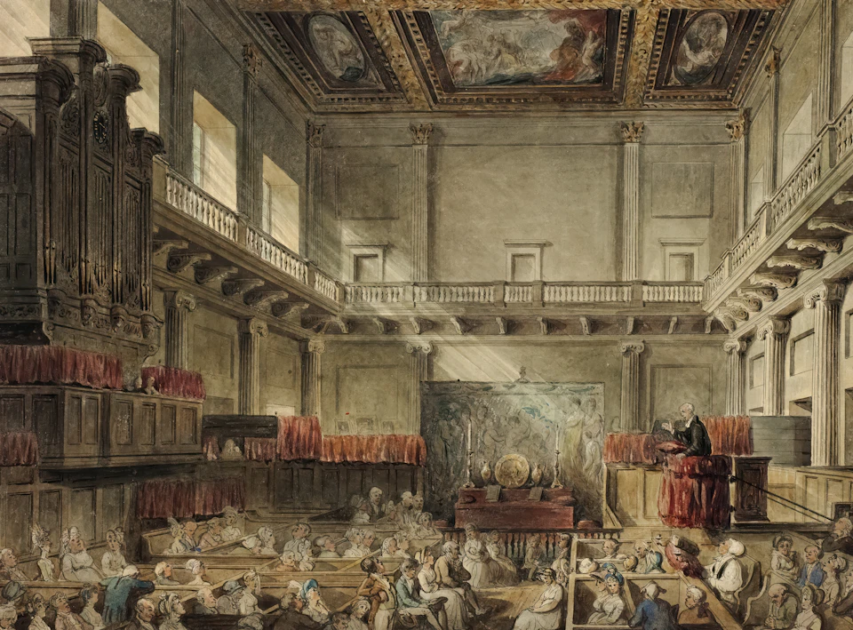 The image depicts a grand, ornate room with high ceilings and large windows that allow natural light to flood the space. The walls are adorned with intricate paintings and decorations, adding to the opulence of the room. A stage is set up in the center of the room, suggesting it may be used for performances or events.

The room is filled with people seated on benches arranged around the stage, facing towards a speaker standing at the front of the room. The audience appears engaged and attentive, indicating that they are likely listening to a speech or performance.