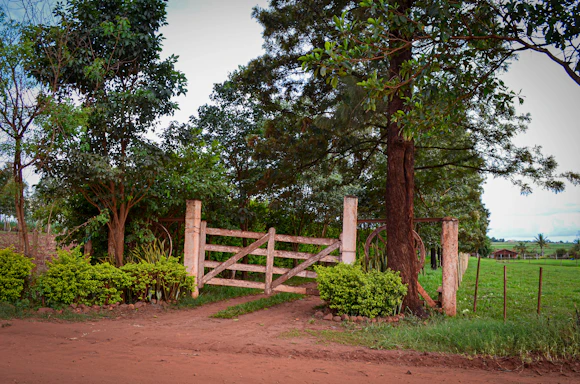 A rustic farm gate opening to green pastures with chickens and fish ponds visible in the background.
