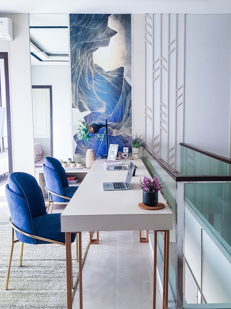 a white table with blue chairs and a painting on the wall